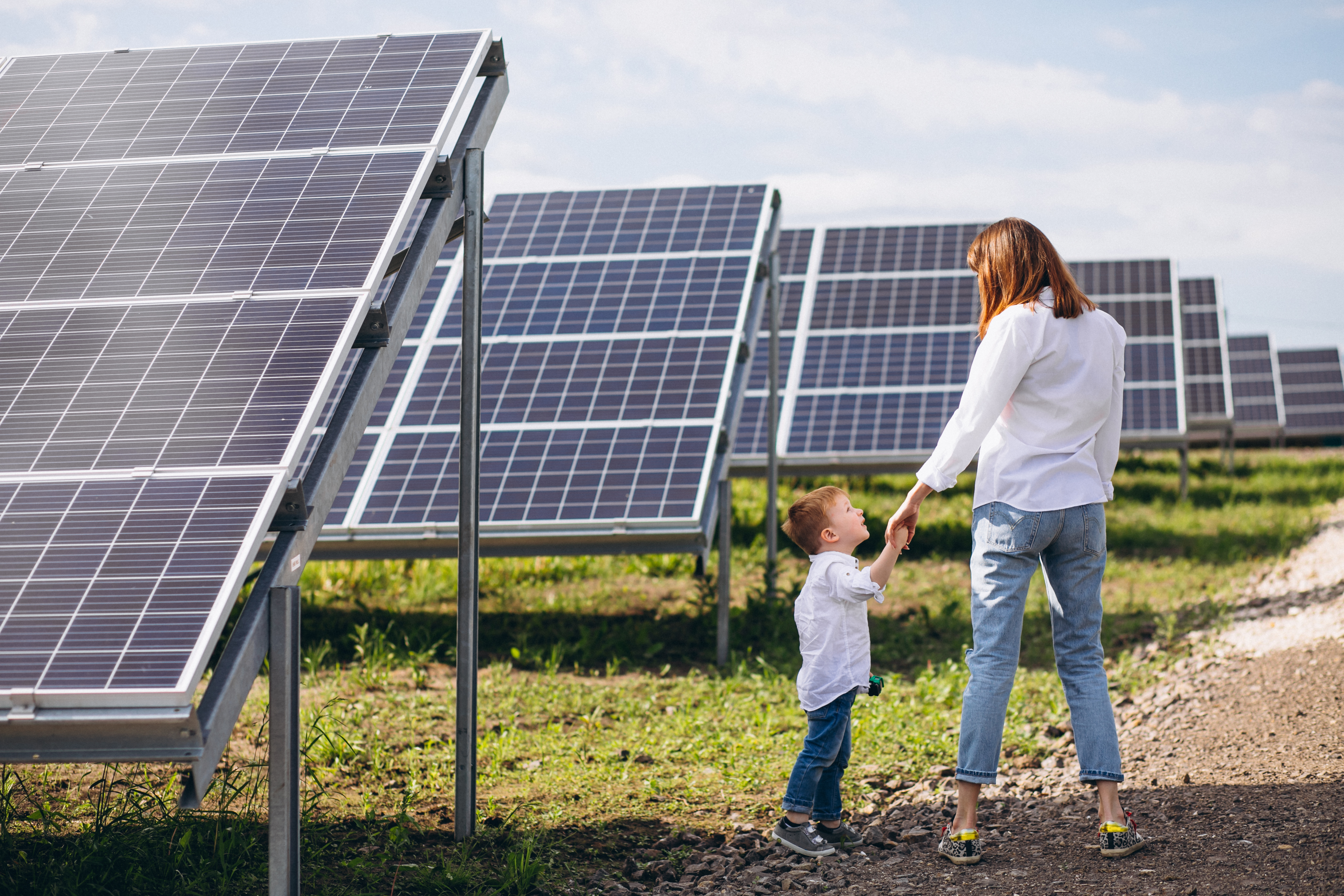Madre con su hijo caminando junto a paneles solares en un campo, s&iacute;mbolo de autonom&iacute;a energ&eacute;tica y futuro sostenible