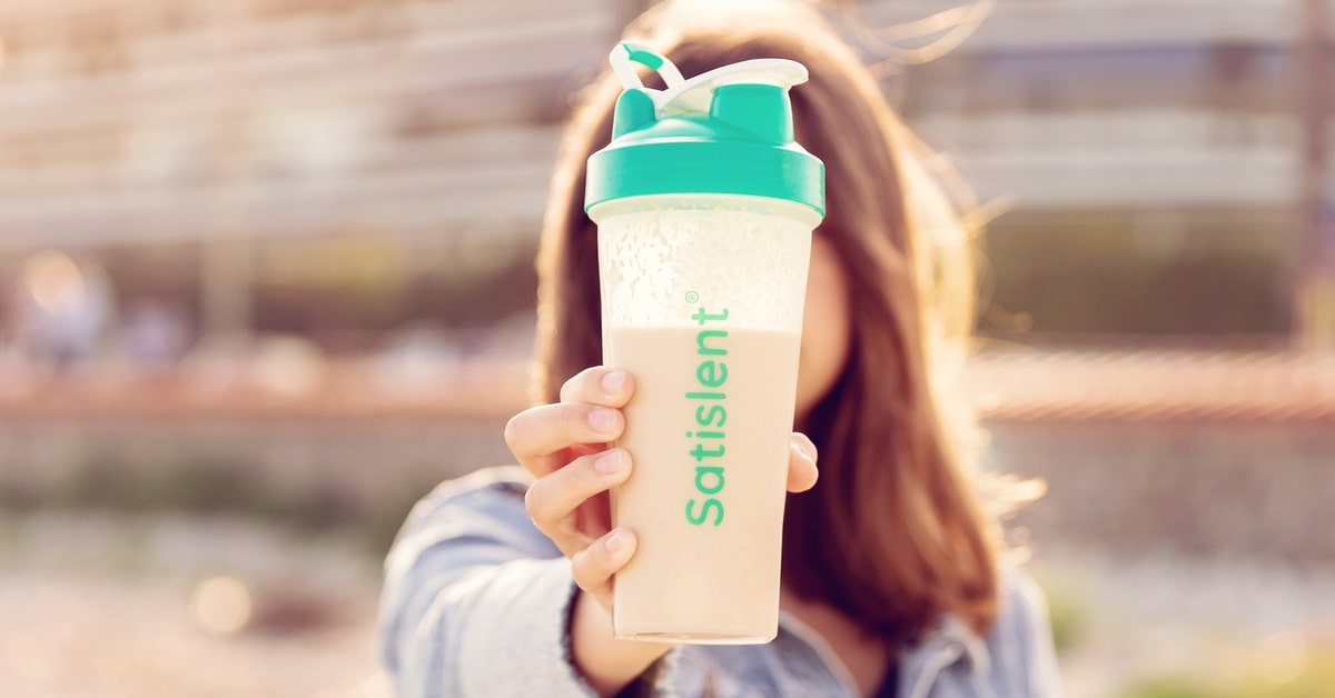Woman holding a Satislent meal shake outdoors, perfect for a healthy breakfast and an energizing morning routine